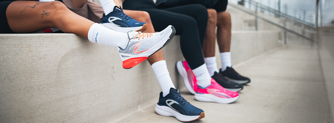 Four people wearing colorful athletic shoes and white socks sit on concrete steps, with their legs extended forward. The focus is on their feet and shoes, not their faces.