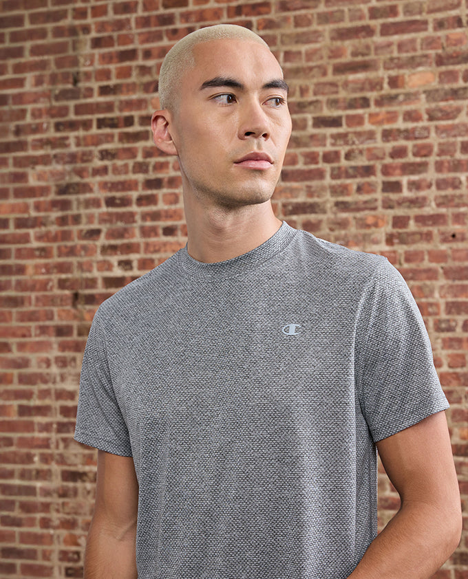 Man wearing a gray Champion t-shirt against a brick wall