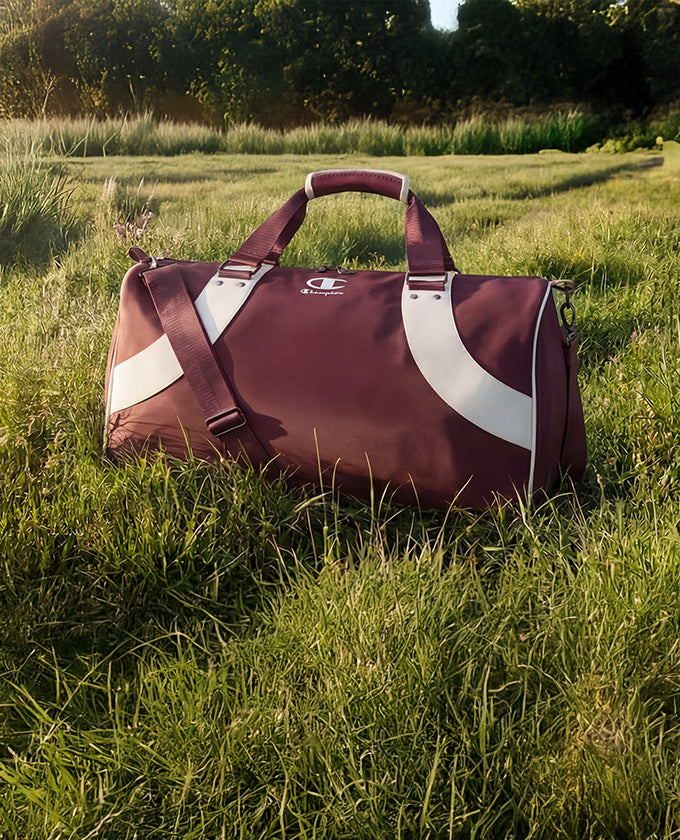 Maroon and white duffel bag on grass with a blurred natural background