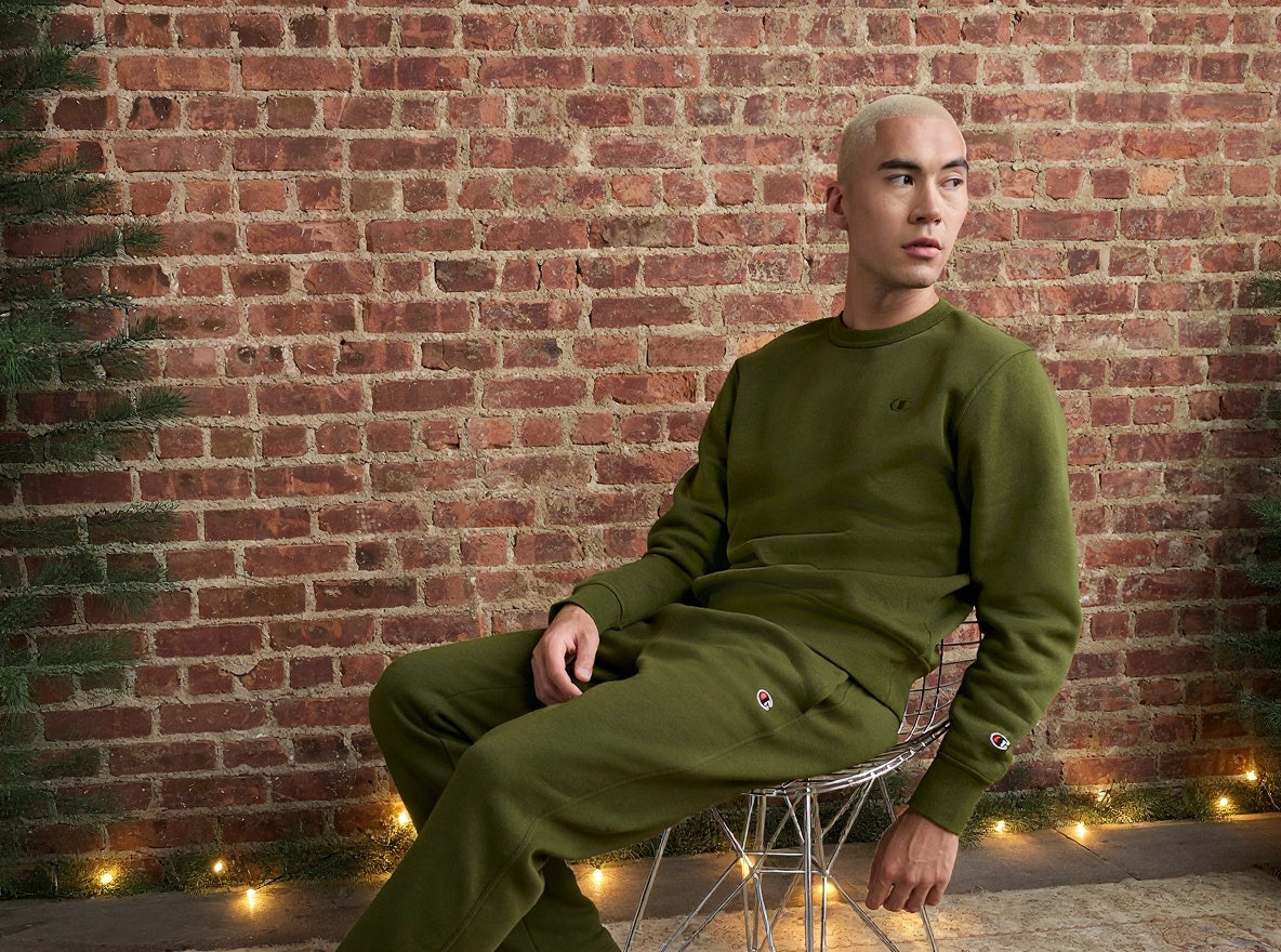 Person wearing a green outfit sitting against a brick wall with decorative lights.