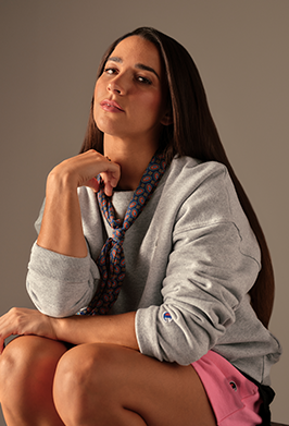 Woman wearing a gray sweatshirt and pink shorts sitting against a plain background