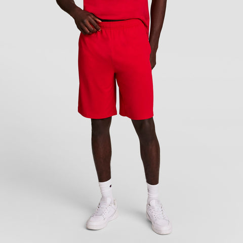 A person poses against a plain background wearing a red T-shirt, Champion 10" Moisture Wicking Sport Shorts, white socks, and white sneakers. The individual’s head is not shown in the image.