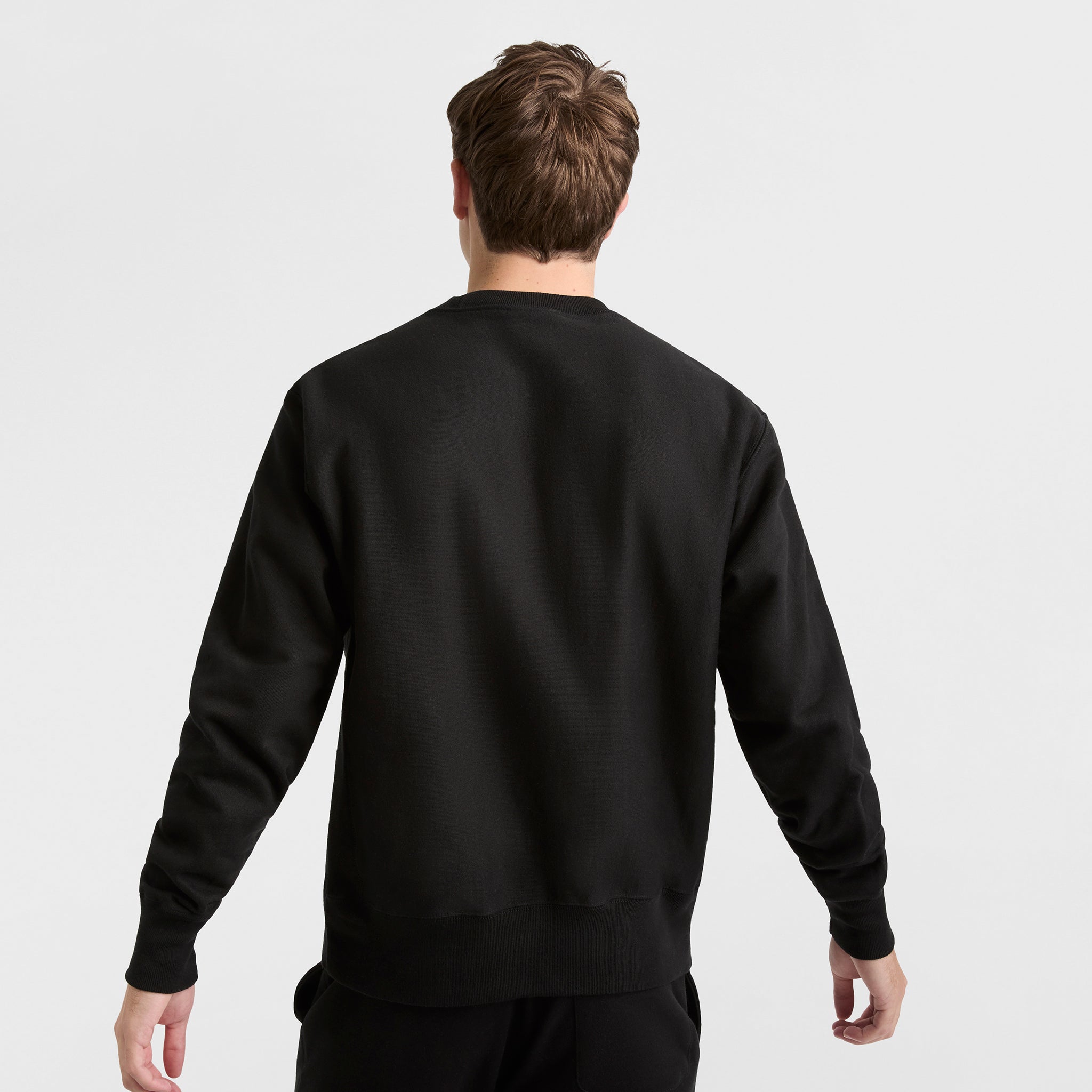 A person with short brown hair is shown from the back wearing a Champion Reverse Weave Crewneck Sweatshirt, C Logo, and black heavyweight fleece pants against a white background.