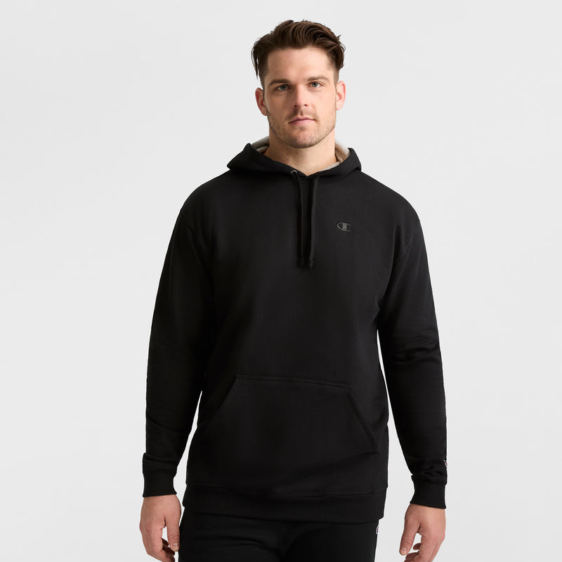 A man faces forward in a plain black Champion Powerblend Hoodie, C Logo - Big & Tall, with a small logo on the left chest and black pants, against a light gray background.
