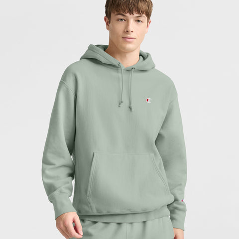 A male model wearing a green Champion hoodie with an embroidered logo, featuring a hood and front pocket.