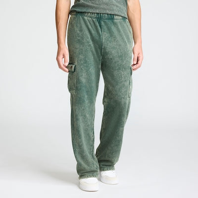 A person wearing loose-fitting, green cargo sweatpants with side pockets and white sneakers, standing against a plain white background. The upper body is partially visible.