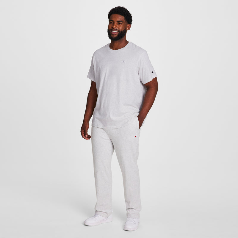 A man smiles, wearing Champion Lightweight Lounge Pants, Open Hem, C Logo - Big & Tall in light grey with a matching Champion T-shirt and white sneakers against a plain white background.