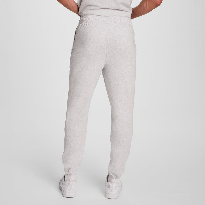 Model wears Champion Lightweight Lounge Pants with cinched hem and C logo, featuring a stretch waistband and elastic cuffs. Shown from the back with hands on hips, paired with white sneakers against a plain white background.