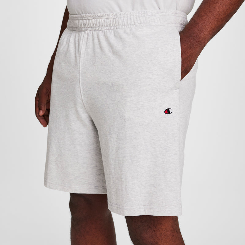 A person wearing Champion 9" Lightweight Lounge Shorts, C Patch Logo - Big & Tall in light gray with an elastic waistband and small logo on the left leg, standing with one hand in their pocket against a plain background.