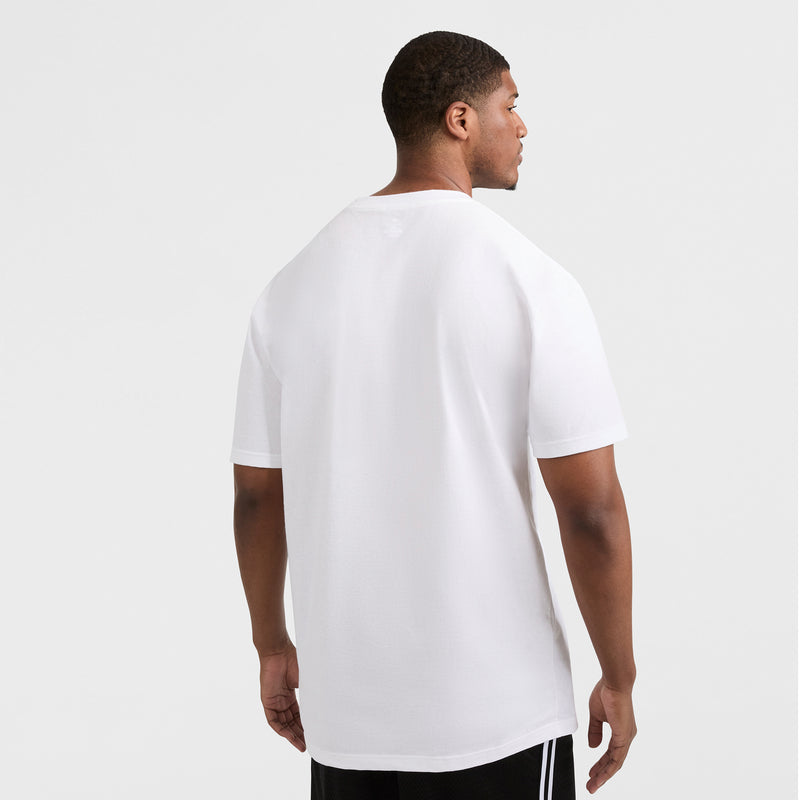 A man stands with his back to the camera, wearing a Champion Classic T-Shirt, C Logo - Big & Tall in white and black shorts with white stripes, set against a light gray background.