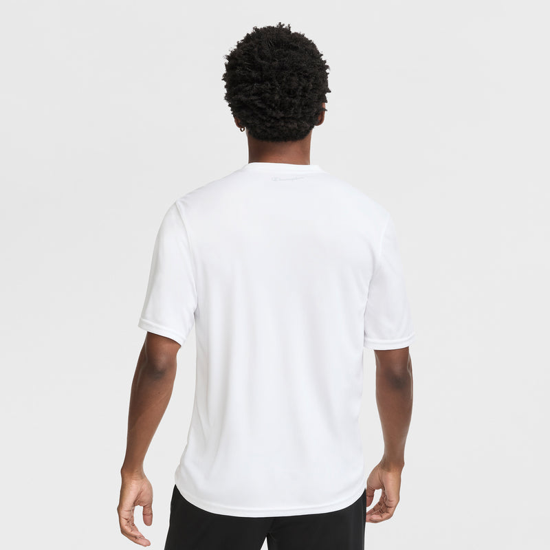 A person with short curly hair faces away from the camera, wearing a Champion Sport T-Shirt with Reflective C Logo and black pants, set against a white background.