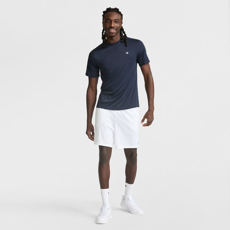 A man with long twisted hair smiles against a plain white background, wearing a Champion Sport T-Shirt with Reflective C Logo featuring Double Dry technology, paired with white shorts, crew socks, and sneakers.