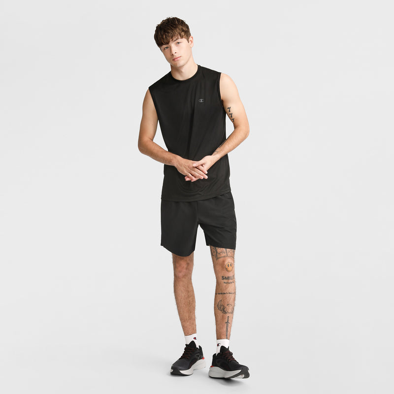 A young man wears the Champion Sport Muscle Tank with Reflective C Logo, paired with black shorts and sneakers. Standing against a white background, he shows off leg tattoos and short hair—an ideal workout shirt for comfort and style.