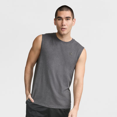 A man with short dark hair wears the Champion Muscle Tank, C Logo, in dark gray with black shorts, standing against a plain white background and posing with one hand in his pocket.
