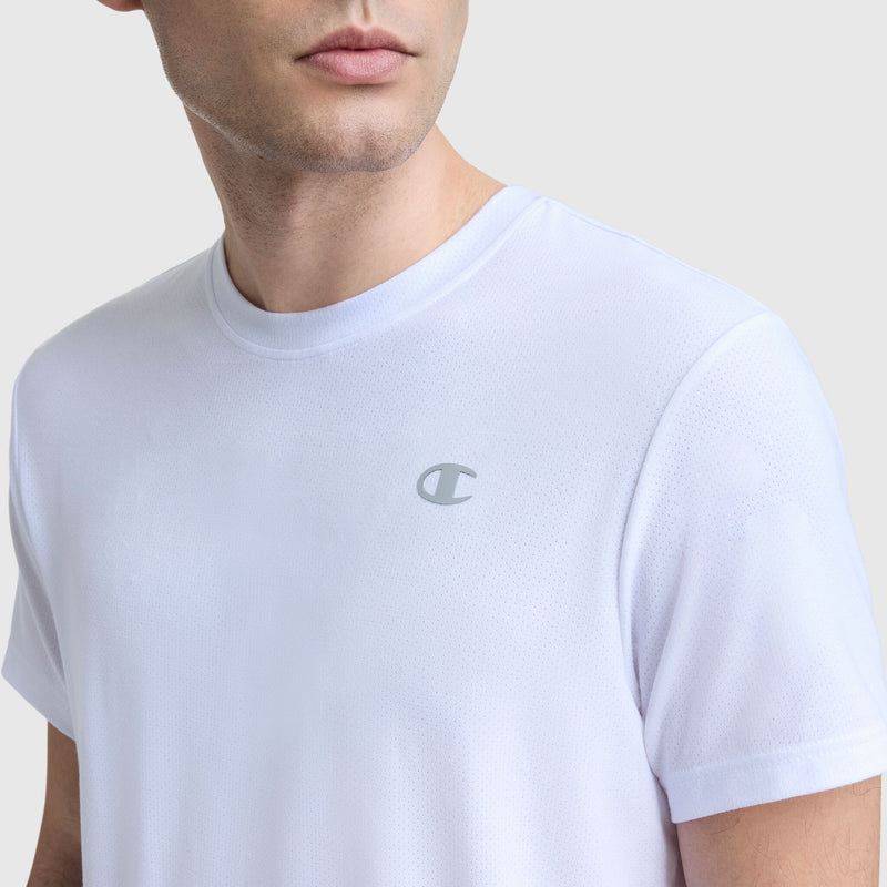 A man wears a Champion Sport Crewneck T-Shirt, Script Logo, a plain white men's slim-fit tee featuring a small script Champion logo on the left chest, shown from the shoulders up against a light gray background.