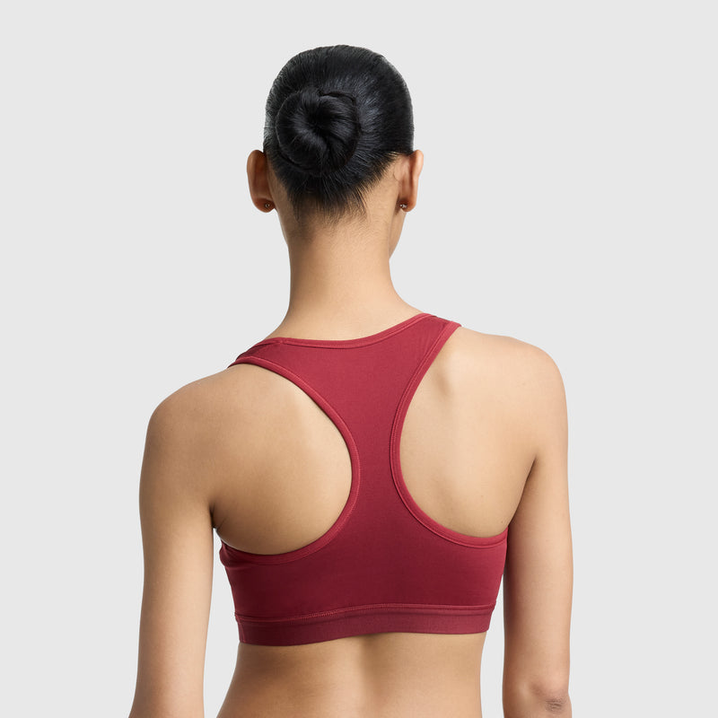 A woman with dark hair in a neat bun is shown from the back wearing the Champion Compression Sports Bra, C Logo, in maroon with a racerback design against a plain light gray background.