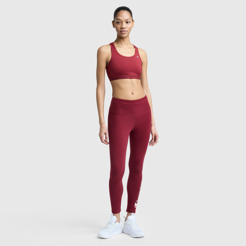 A woman faces forward in a maroon Champion Compression Sports Bra (C Logo) with matching high-waisted leggings and white sneakers, set against a plain light gray background.