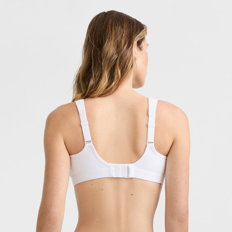 A woman with long, wavy hair is shown from the back wearing the Champion Spot Comfort High-Impact Sports Bra, C Logo, featuring wide adjustable straps and a hook-and-eye closure against a plain light background.