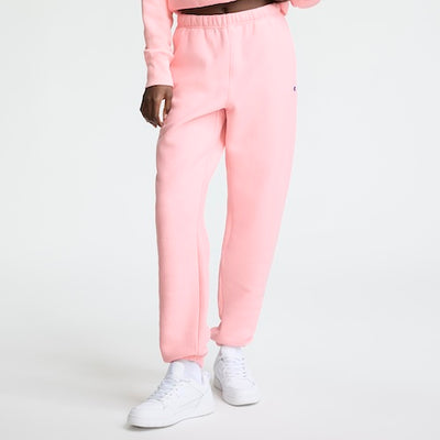 A person wearing light pink sweatpants, a matching pink sweatshirt, and white sneakers stands against a plain white background. The photo is cropped above the waist.