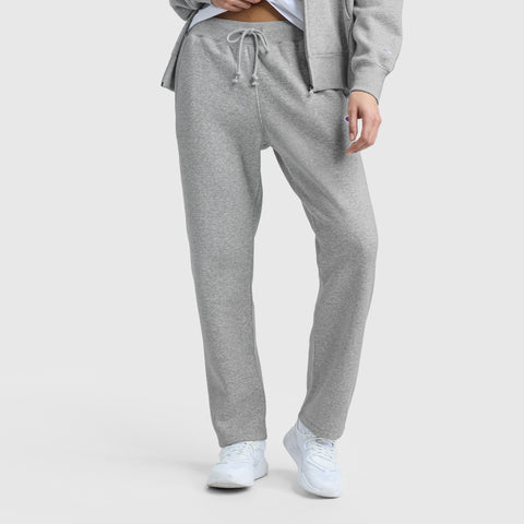 A person stands against a plain light background, shown from the shoulders down, wearing Champion Powerblend Straight Hem Sweatpants in light gray fleece with a matching zip-up hoodie and white sneakers.