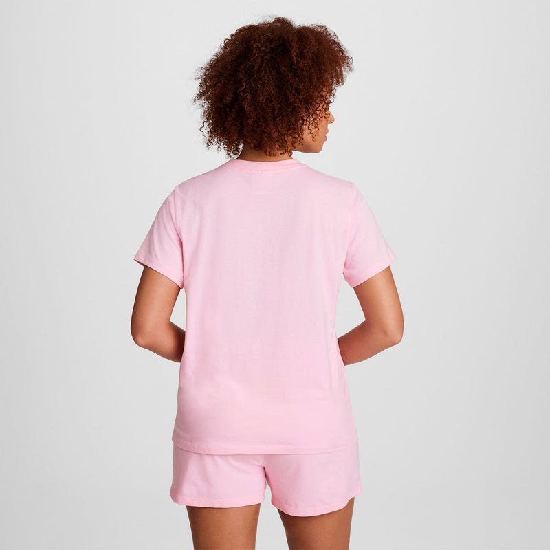 A person with curly hair, seen from behind against a plain light background, wears a Champion Classic T-Shirt with Tonal Left Chest Script in light pink and matching pink shorts.