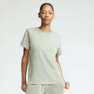 A person stands against a plain light background, wearing a light sage green t-shirt and matching pants, with a relaxed pose and a neutral expression.