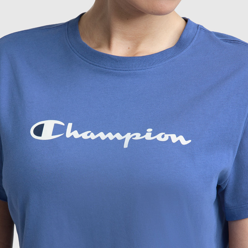 A person wears the Champion Classic T-Shirt, featuring the white script logo across the chest. This crewneck tee offers a comfortable fit, and their face is partially out of frame.