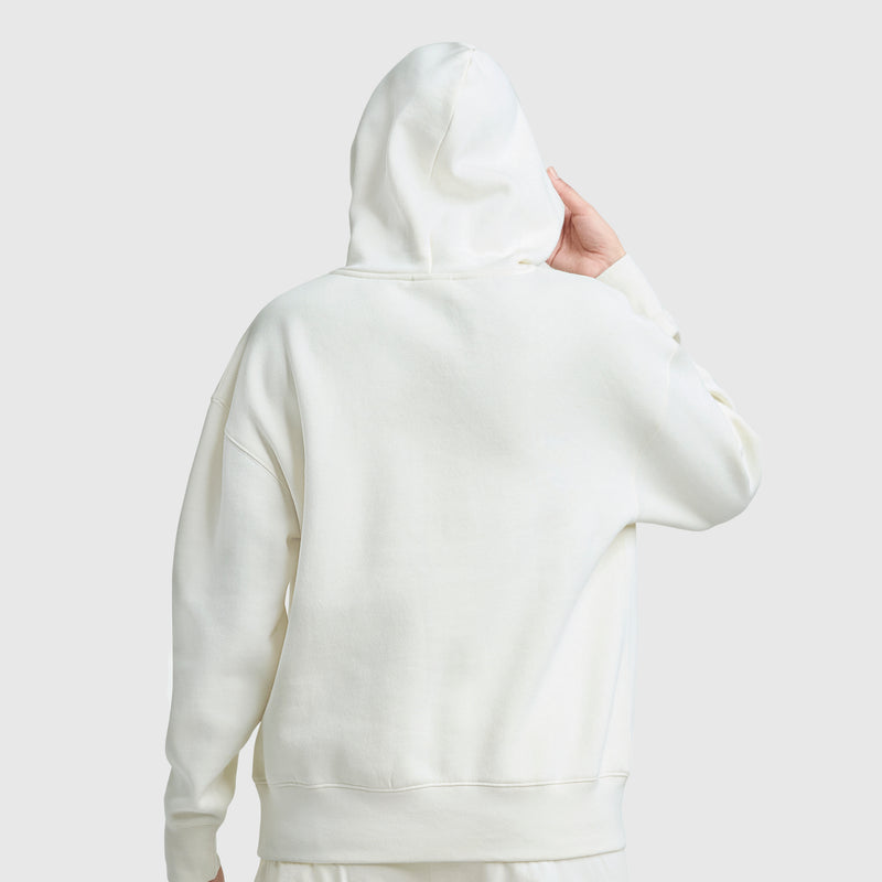 A person wearing a Champion Tonal Script Freshman Powerblend Hoodie, off-white women's pullover style, is seen from behind touching the hood against a plain light gray background.