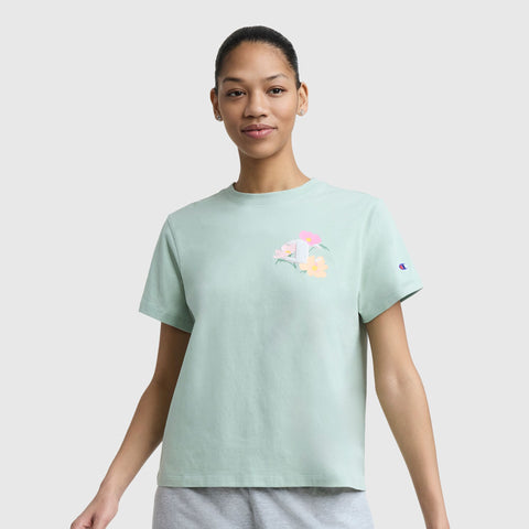 A person faces forward in a light green Floral Mesh "C" Graphic T-Shirt by Champion, featuring a small colorful "C" floral logo on the chest, paired with light gray shorts, set against a plain light background.