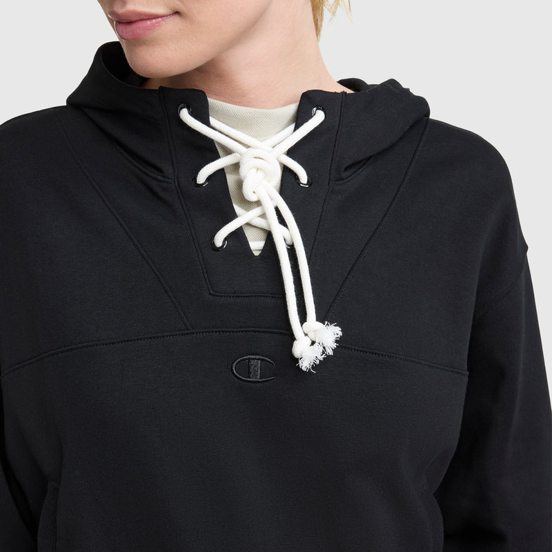 A person wears a black Champion Tackle Lace Front Hoodie with white lace-up drawstrings tied at the neck. The hoodie features a tonal embroidered C logo on the chest. Only the lower half of the face and upper torso are visible.