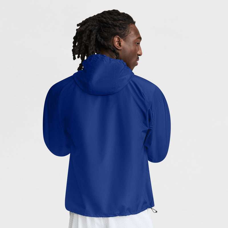Seen from behind, a person with medium-length dreadlocks wears the Champion Stadium Packable Jacket with Script Logo in royal blue and white shorts, standing against a plain white background.