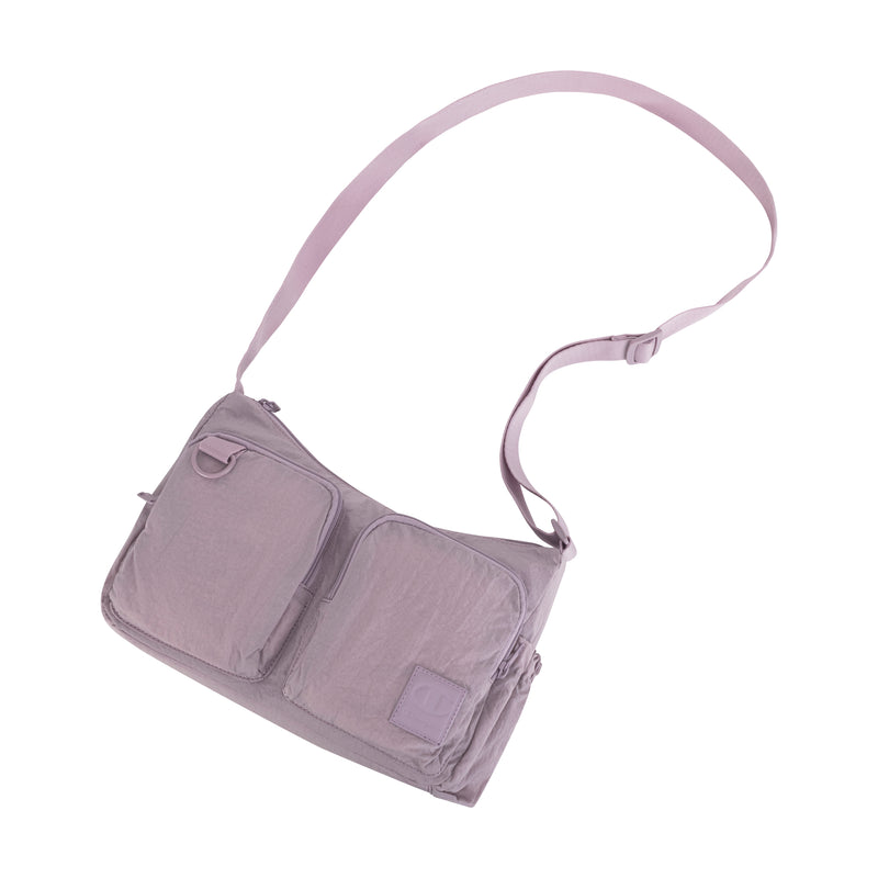 The Champion Quartz Small Messenger Bag features a light purple color, two front zippered pockets, an adjustable shoulder strap, and a minimalist design for hands-free convenience. Shown on a white background.