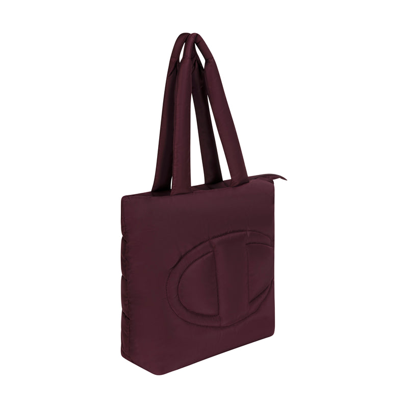 The Champion Quilted Billie Tote features double handles, a large stitched oval logo on the front, and comes in dark burgundy—a stylish choice for everyday use. Shown on a white background.
