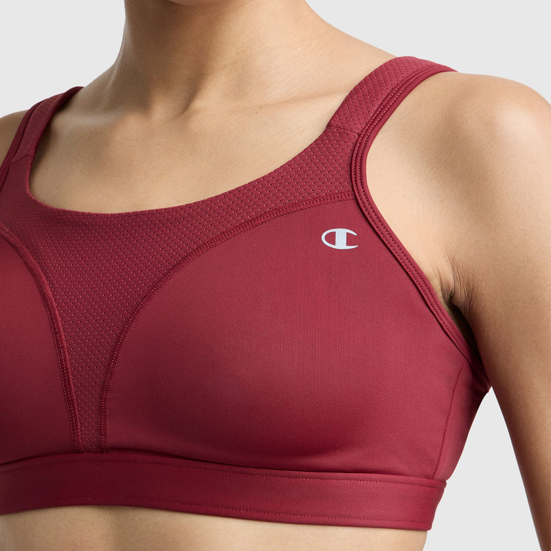 A person wears the Champion Spot Comfort High-Impact Sports Bra with mesh detailing and a small white C logo on the left, set against a neutral light gray background. The image highlights the upper torso and shoulders.