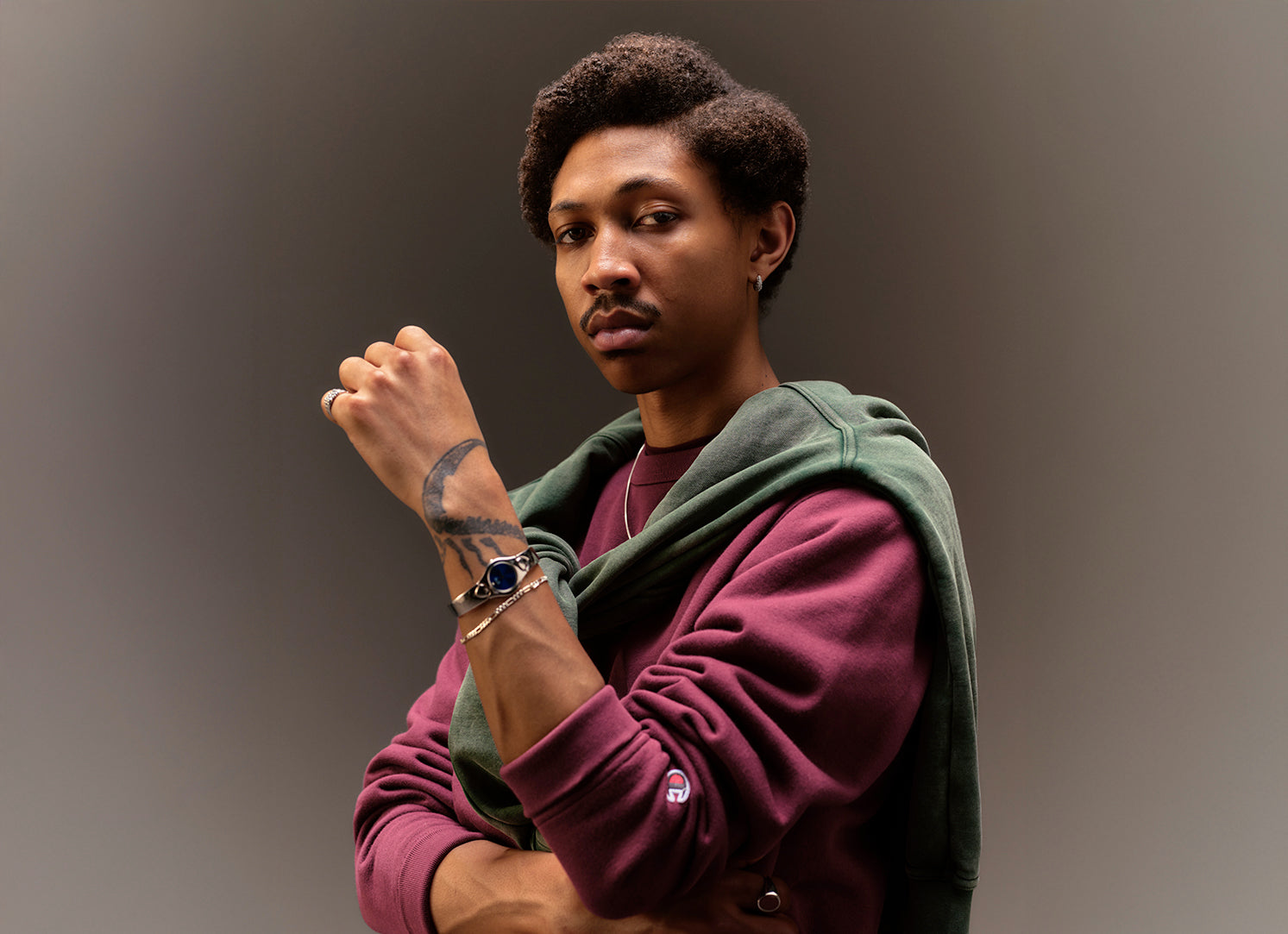 Man wearing a maroon sweatshirt and green sweatshirt overlayed against a gray background