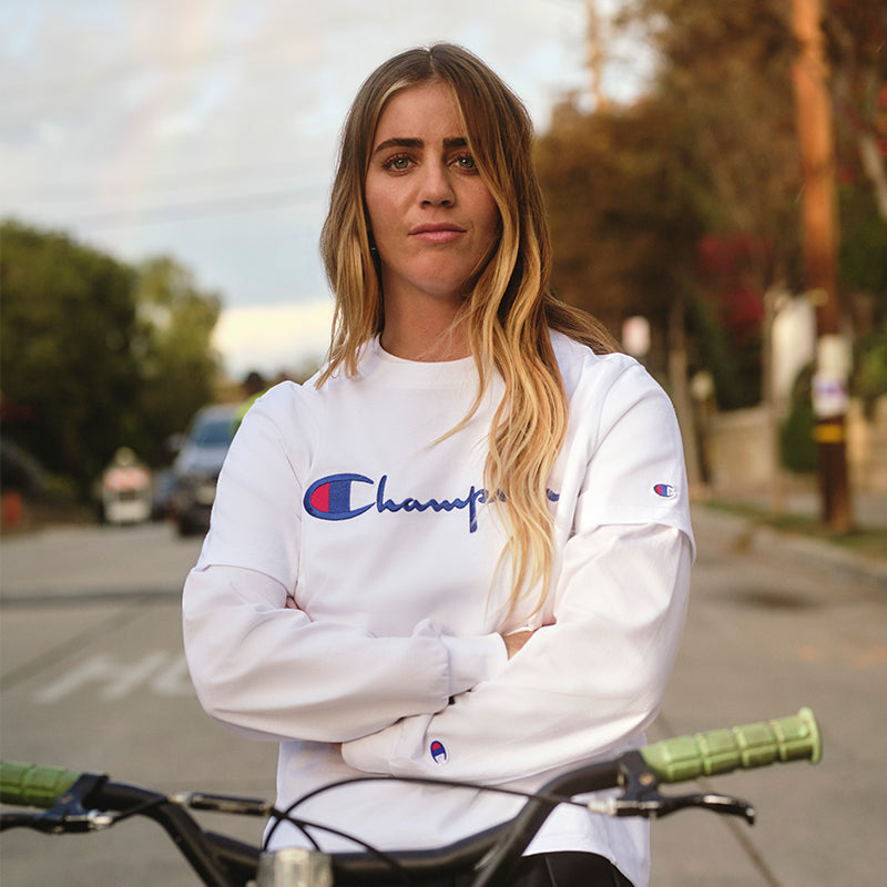 Person wearing a white Champion sweatshirt standing outdoors with a bicycle.