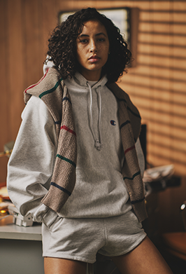 Person wearing a gray hoodie and shorts with a plaid jacket over shoulders indoors.