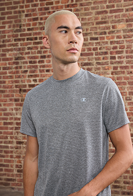 Man wearing a gray Champion t-shirt against a brick wall